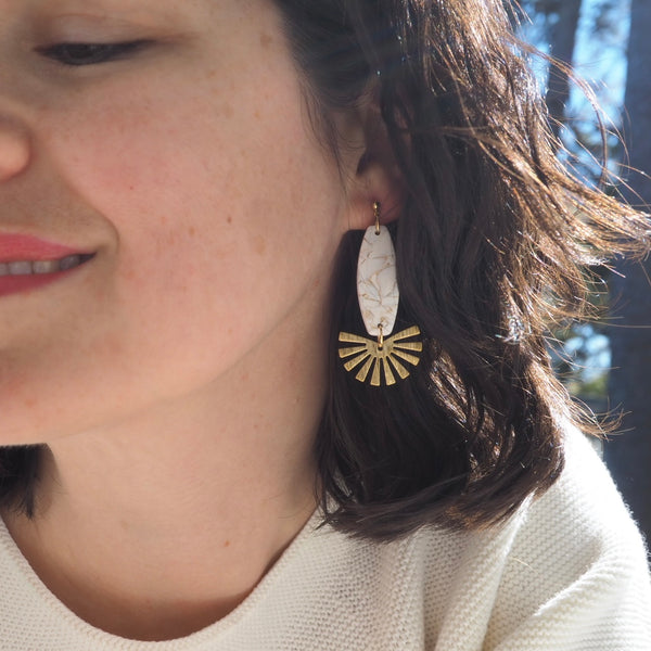 Close-up of a model wearing white and gold faux marble dangle earrings handmade with polymer clay with brass components